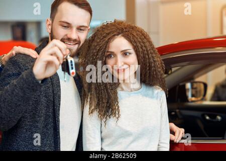 young couple has bought a car, close up photo. man presenting a car for his woman. close up photo. red car in the background of the photo Stock Photo