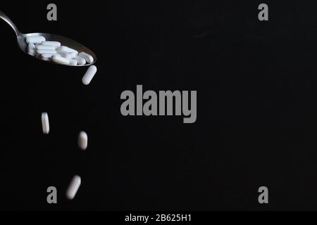 White pills poured out of spoon like liquid medicine with black background Stock Photo