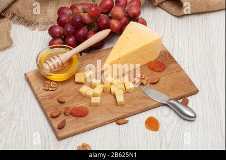 Cheese on a board with honey, nuts, dried apricots, grapes Stock Photo
