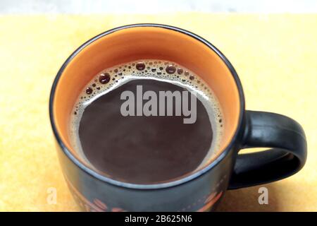 Black mug with coffee orange inside with a pen and a pattern standing on a white background top view. Stock Photo