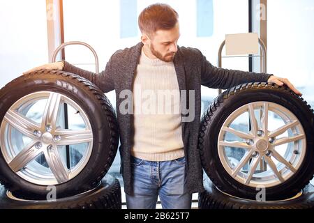 pleasant bearded man touching and choosing for buying a tire in a supermarket shop or DIY department store, close up photo. Stock Photo
