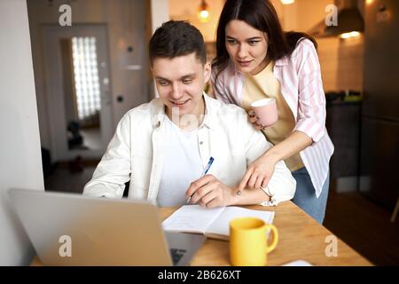attractive loving couple looking at the laptop in the kitchen, drinking tea, close up photo. free time, spare time, lifestyle Stock Photo