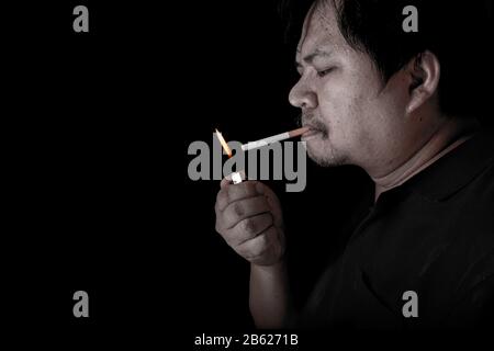 The fat man lighting up a joint with lighter smoking at the black background, close up image of cigarette smoke spread in hand Stock Photo