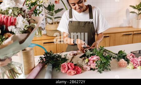 Smiling florist preparing a flower bouquet at her shop. Woman in apron working at counter. Stock Photo