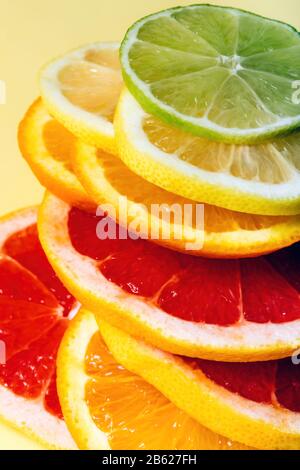 Citrus lemon, lime, orange and grapefruit slices in pile on yellow background. Minimal design background. Stock Photo