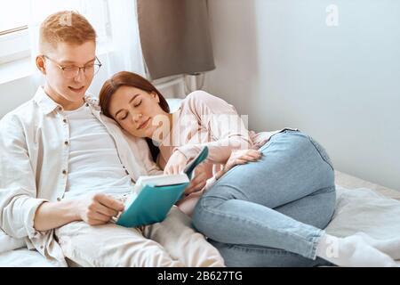 young man in glasses enthusiastic about reading a novel while his girlfriend is sleeping, lying with closed eyes, relaxation . close up photo Stock Photo