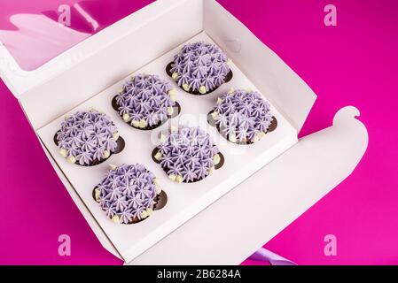 Delicious shawn cupcakes with curd cream in the form of flowers on a pink background. White cupcake packaging. Stock Photo