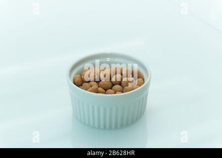Roasted salty peanuts on white background with copy space. Japanese peanuts in a white ceramic bowl on a white table. Selective focus. Stock Photo