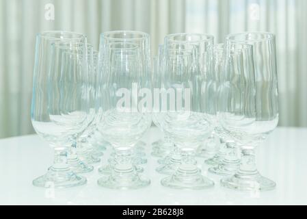 Empty crystal glasses side by side on white table. Collection of various glasses for water and juice isolated on white, front view. Empty glasses. Stock Photo