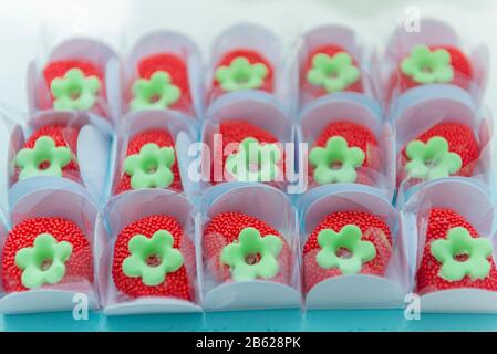 Strawberry shaped children's party sweets. Red sprinkled candies in white paper box on blue tray with shallow depth of field. Selective focus. Stock Photo