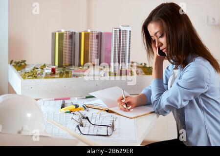 beautiful young awesome female architect drawing model in the paper. close up side view photo.luxury breadboard model in the background of the photo, Stock Photo