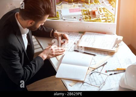 Successful attractive male engineer drawing house draft, man in official clothes sitting at the the table and measuring scetch,top side view photo Stock Photo