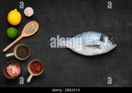 Overhead view of fresh raw gilt head bream with spice on black stone background Stock Photo
