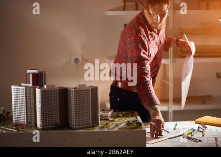 bearded designer holding paper , looking at the blueprint analizing, checking drafts while standig behind the table. close up photo. copy space , busy Stock Photo
