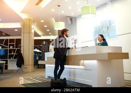 friendly female receptionist greeting a client, tourist, close up side view photo, businessman checking in at a hotel Stock Photo