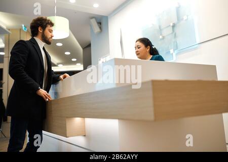 smiling friendly female receptionist in hotel giving advice to guest, close up side view . custumer paying at the hotel with a credit card Stock Photo