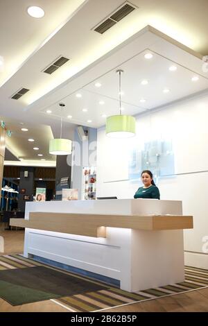 friendly female receptionist worker standing at luxury hotel counter, waiting for guests. close up side view photo, job, profession, occupation Stock Photo