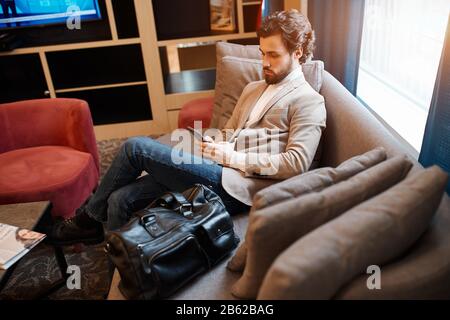 young attractive man in stylish casual clothes relaxing on the luxury comfortable sofa, using gadget, close up side view photo. man doing shopping onl Stock Photo