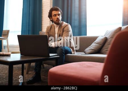 Young handsome man working on laptop at the aiport, looking aside, away, businessman surfing, browsing the net while waiting for the flight, plain. cl Stock Photo