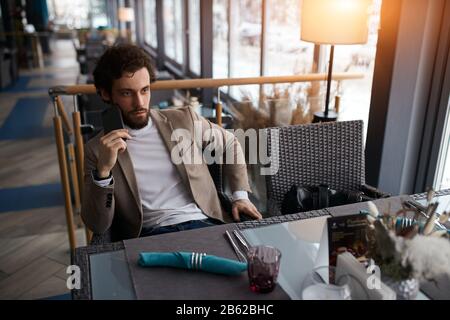 Young serious man making a phone call in coffee shop, sitting at the table, solving business problem. close up photo Stock Photo