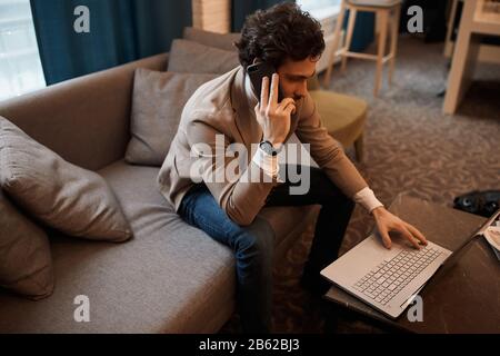 young man in casual stylish clothes sitting on the sofa and surfing the net, close up side view photo, job, profession, occupation, freelancer working Stock Photo