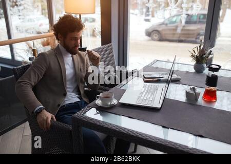 Business man having serious expression, sitting at the table looking at the laptop, puzzled worried businessman solving problems, close up side view p Stock Photo