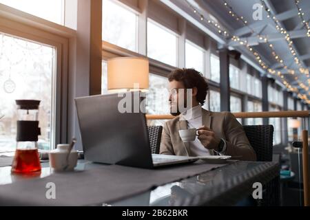 young serious man looking at the window, holding a cup, businessman having breakfast in the restaurant. good morning. lunch time Stock Photo