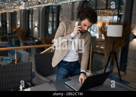 young manager talking on smart phone, texting message on laptop, close up photo. guy serfing, browsing the net, internet Stock Photo