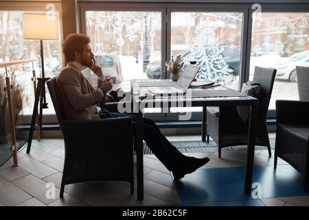 smart businessman sitting on the chair, touching his lips with fingers, trying to overcome problems, making decision, full length side view photo. Stock Photo