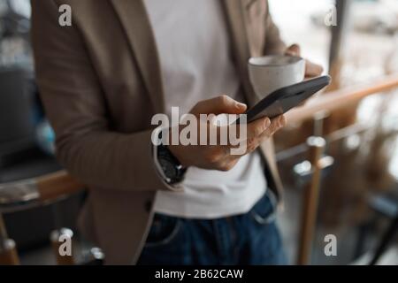 young man in casual fashion clothes holding smart phone and texting message, sms, close up cropped photo. guy searching wi-fi connection, internet Stock Photo