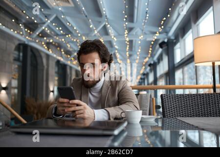 serious guy having a rest at the cafe, watching video, movie, film, close up photo. student reading e-book in the cafe Stock Photo