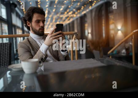 serious elegant guy using his smart phone while having a rest at the cafe. close up photo. free time, spare time, lifestyle , blurred foreground, tech Stock Photo
