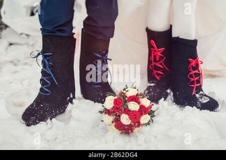 A closeup of the feet of the bride and groom in felt boots on snow wedding bouquet. Accessories for a stylized Russian wedding. Stock Photo