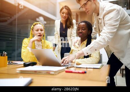 young clever computer hacker overcoming problem, computer expert teaching woman to work with programme, coworkers sending e-mail, sms, chatting with p Stock Photo