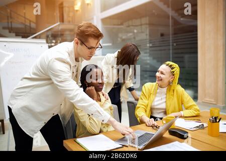 computer programmer in glasses fixing, mending computer, downloading antivirus system, afro woman has problems with computer, two women laughing in th Stock Photo
