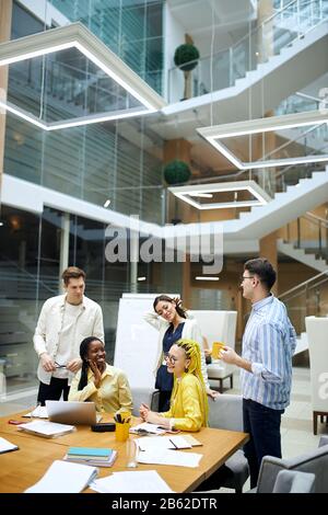 young positive cheerful people having free time at workplace, vertical shot. break time, friendly conversation among co-workers Stock Photo