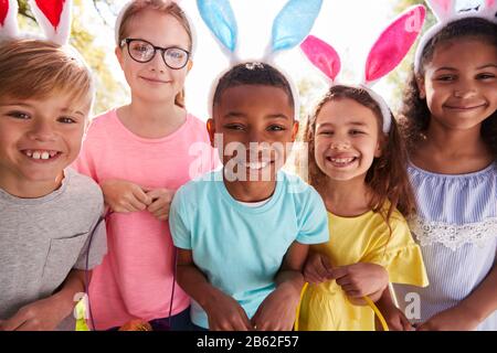 Portrait Of Five Children Wearing Bunny Ears On Easter Egg Hunt In Garden Stock Photo