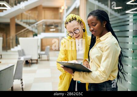 two clever ambitious women concentarted on analyzing financial figures on a graphs on papers in modern office, close up side view photo. Stock Photo