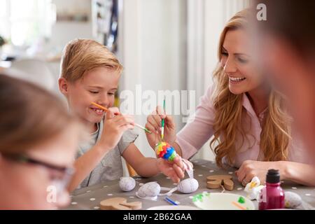 Parents With Children Sitting At Table Decorating Eggs For Easter At Home Stock Photo