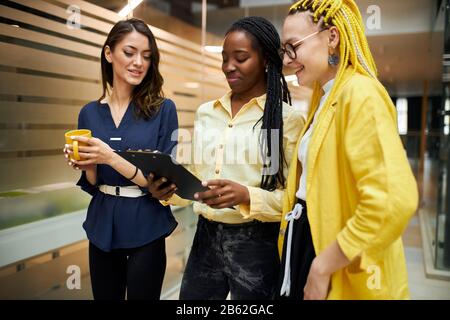 attractive three friends in casual stylish clothes checking the document, drinking tea, spending time, free time, lifestyle, spare time at work , frie Stock Photo