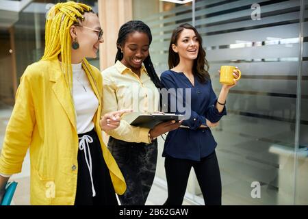 cheerful young businesswomen having fun while walking in the office building, careless life, successful employees laughing, amiling, having a rest aft Stock Photo