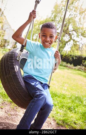 Portrait Of Smiling Boy Having Fun Playing On Tire Swing In Garden Stock Photo