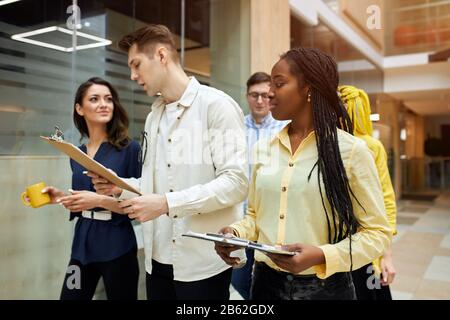 active ambitious people in stylish fashion clothes discussing documents. handsome fair-haired male leader giving directions, recommendations to his pa Stock Photo