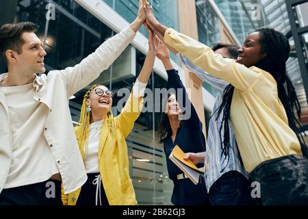 smiling axcited colleagues holding hands, arms together, begging , promising to help each other in any situation, low angle view Stock Photo