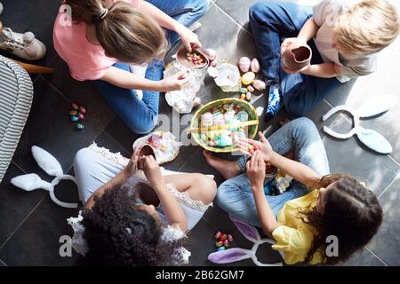 Group Of Children Sitting On Floor At Home Eating Chocolate Eggs They Have Found On Easter Egg Hunt Stock Photo