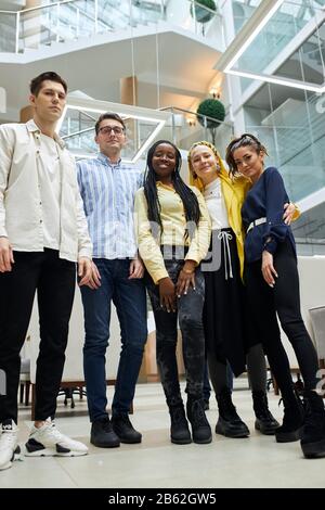 Group portrait of multiethnic young cheerful business people smiling in office, full length photo, partnership, team, friendship. low view Stock Photo