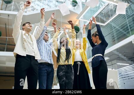 overjoyed young employees and their leader enjoying success, throwing paper, documant, contract. positive feeling and emotion Stock Photo