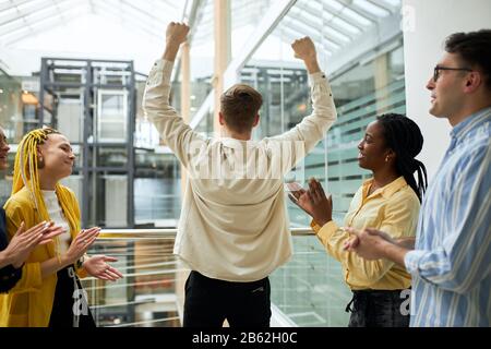 man standing opposite panoramic view with arms up. Happy mixed arce colleagues are clapping their hands, celebrating the performance of new product Stock Photo