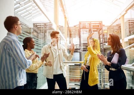 cheerful pleasant young people in fashion clothes having fun in the hall of office, glass wall, celling in the background of the photo Stock Photo