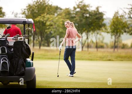 Rear View Of Couple Getting Out Of Golf Buggy To Play Shot On Green Stock Photo